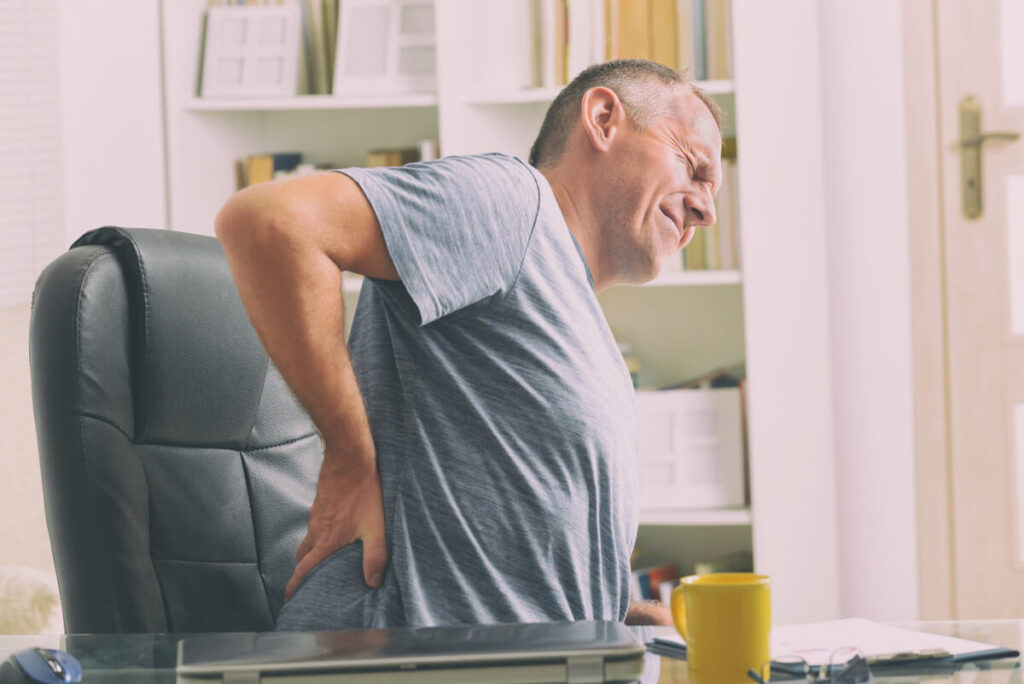 man sitting in chair and holding lower back while in pain